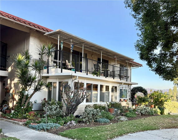 Front view of a two-story house with a covered balcony and landscaped garden.