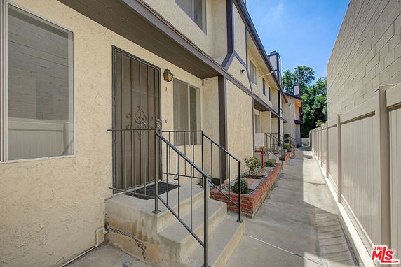 Front view of a multi-story apartment building with metal railings and a narrow entrance path.