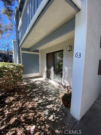 Exterior view of a building entrance with a sliding glass door and number 63 on the wall.