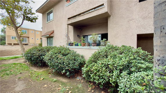 Front view of a residential building with plants and a window balcony.