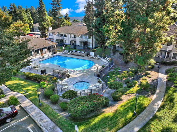 Aerial view of a residential complex featuring a large outdoor swimming pool and hot tub, surrounded by greenery and pathways.