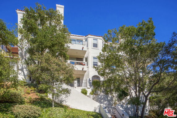 Front view of a multi-story residential building with balconies and trees in front.