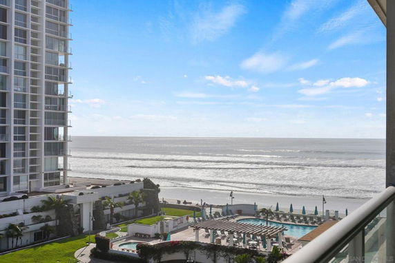 View of the ocean with waves, a pool area, and part of a tall building in the foreground.