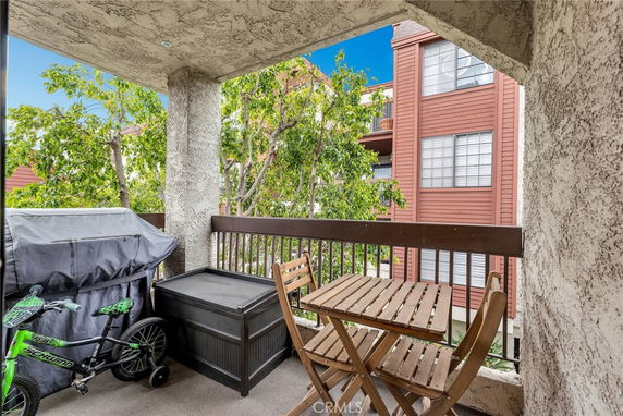 A balcony view featuring a table, chairs, covered grill, and nearby red building.