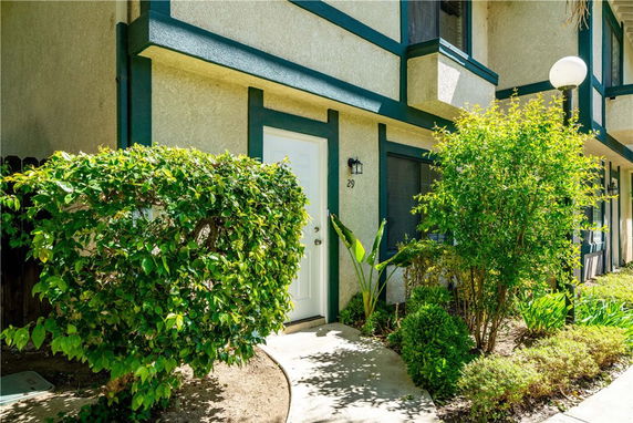 Front view of a house with green trim and white door, surrounded by bushes.