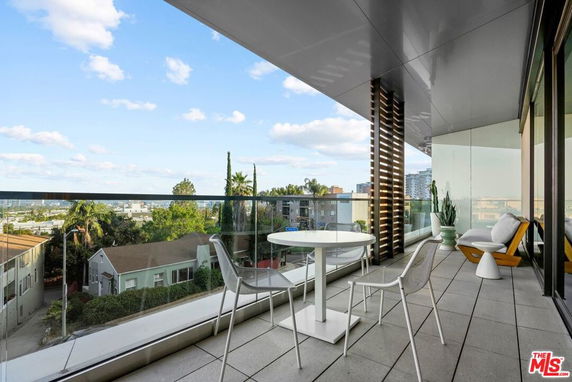 Outdoor balcony with chairs and table overlooking cityscape.
