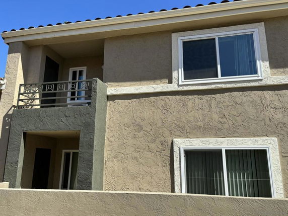 Front view of a two-story house with textured walls and a small balcony.