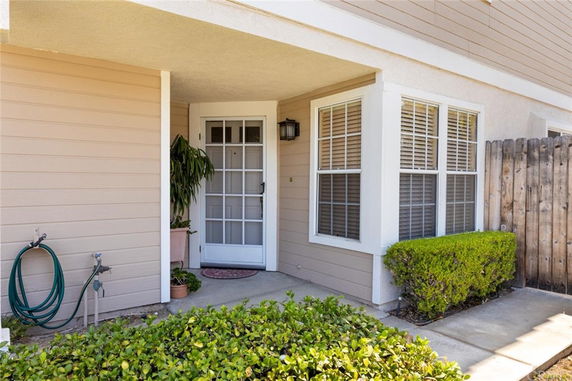 Front view of a house entrance with a glass door and adjacent window, surrounded by shrubbery.