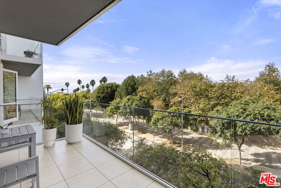 Panoramic view from a balcony with glass railings overlooking trees and a park.