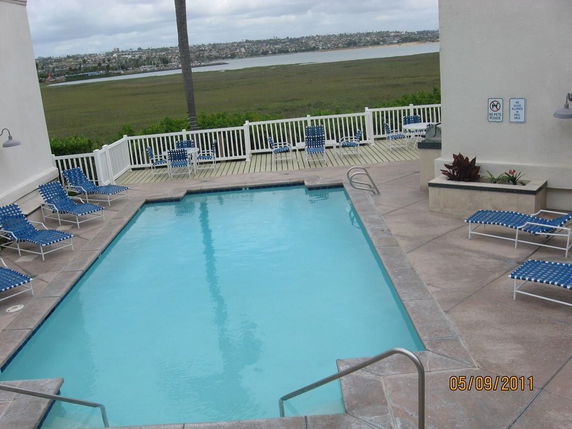 Outdoor swimming pool with surrounding deck chairs and a view of water and distant cityscape.