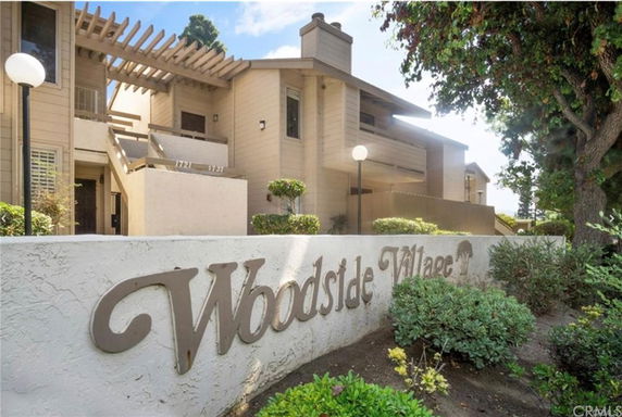 Front view of a multi-story residential building with balconies and an entrance area, labeled Woodside Village.