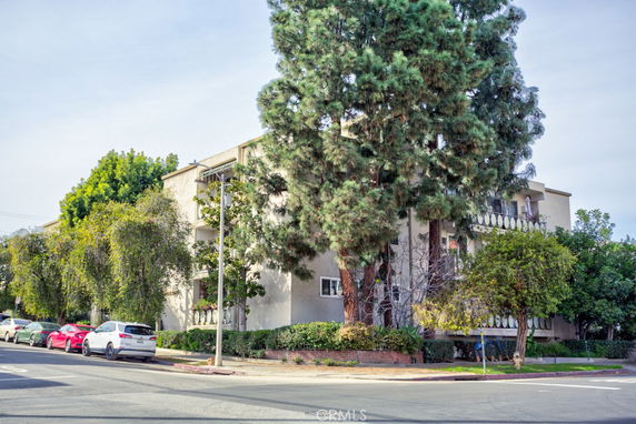 Front view of a multi-story residential building with balconies and surrounded by trees.