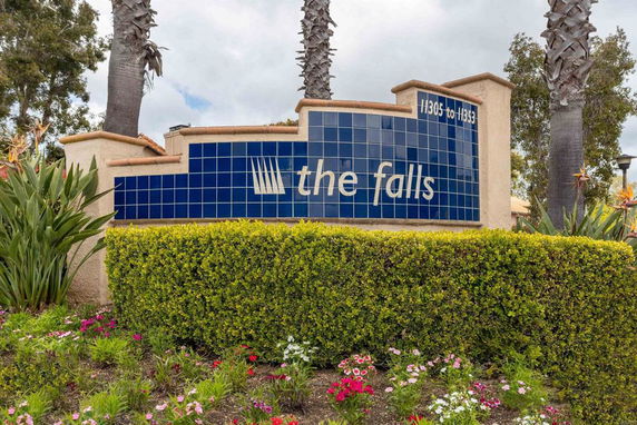 Sign with the name 'the falls' on a decorative wall with blue tiles, surrounded by hedges and plants.