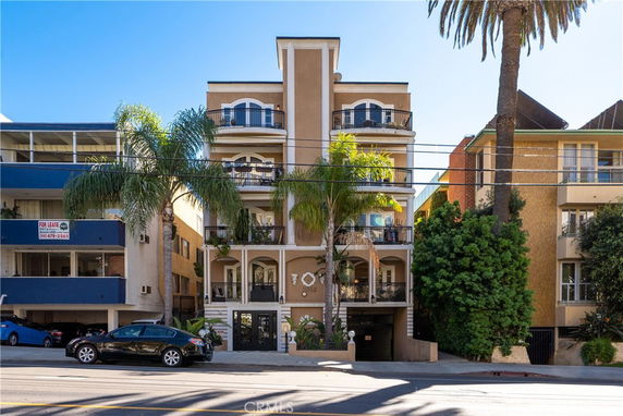 Front view of a multi-story apartment building with balconies and palm trees.