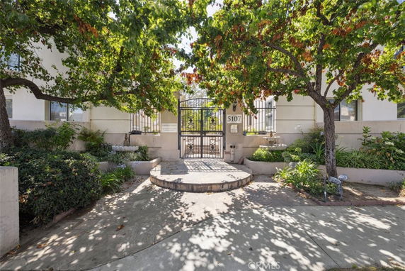 Front view of a building entrance with a metal gate, surrounded by greenery and trees.