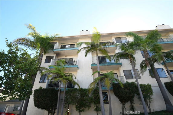 Front view of a multi-story residential building with balconies and palm trees.