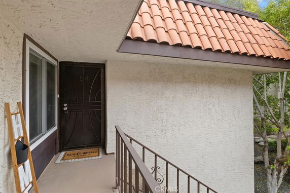 Entrance view of a house with a tiled awning, a dark front door, and a welcome mat.