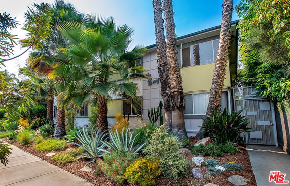 Front view of a two-story house with large windows and surrounding palm trees.
