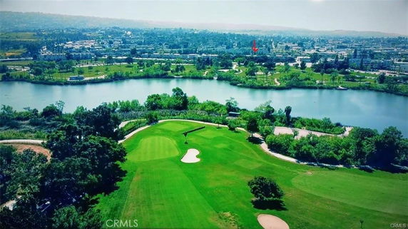 Panoramic view of a landscape featuring a golf course, a lake, and a distant cityscape.
