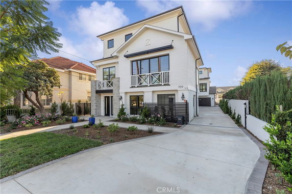 Front view of a modern multi-story house with a paved driveway.