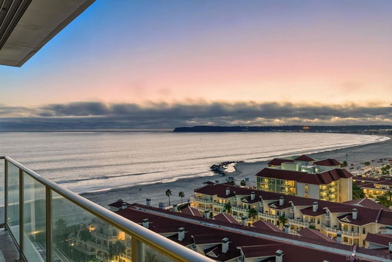 Wide angle view from a building balcony overlooking a beach and ocean at sunset.