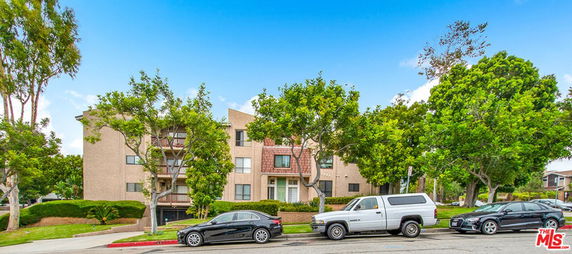 Front view of a multi-story residential building with balconies and parking area in front.