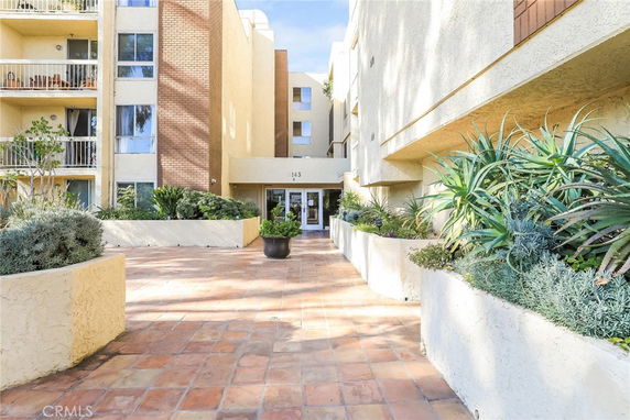 Front view of a multi-story apartment building with balconies and an entrance walkway.