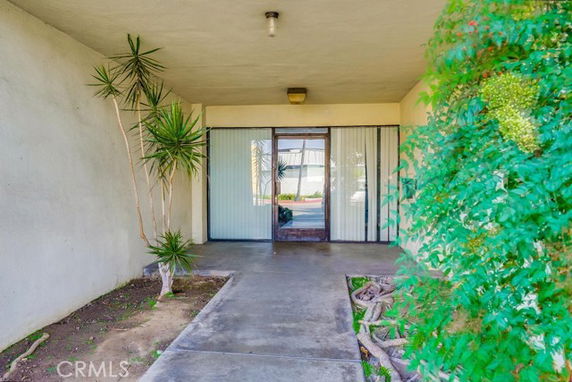 Front view of a building entrance with sliding glass doors and plants on either side.