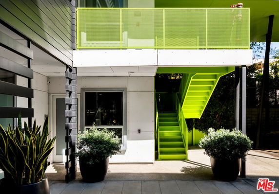 Exterior view of a building with a lime green staircase and railing, adorned with large potted plants.