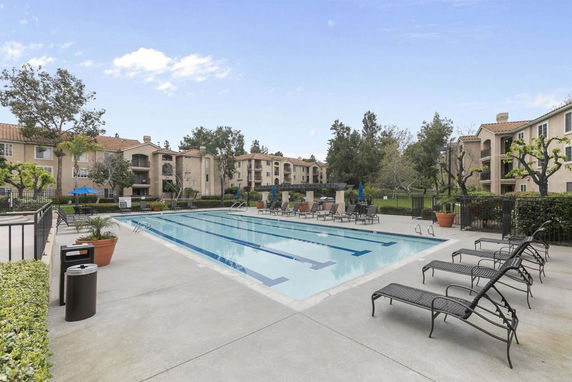 Outdoor swimming pool area with lounge chairs surrounded by apartment buildings.