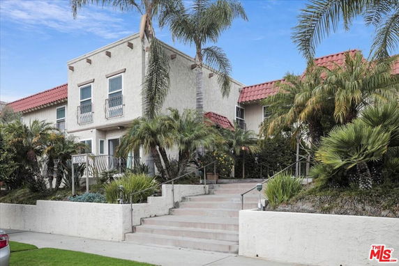 Front view of a two-story house with red-tiled roof and palm trees.