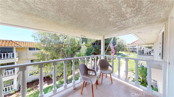 View from a balcony with chairs overlooking a landscaped area and neighboring buildings.