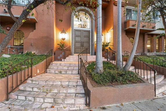Front view of a multi-story building with a grand entrance featuring steps and decorative plants.