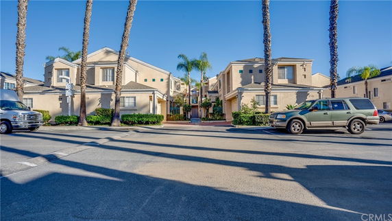 Front view of a multi-story residential building with a light brown facade and palm trees nearby.