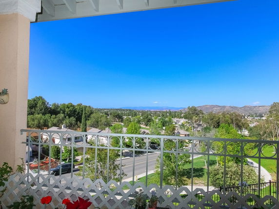 Panoramic view from a balcony showing houses, trees, and distant mountains.