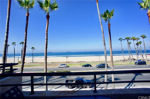 Beachfront view with palm trees, ocean, and sandy shore seen from a building.