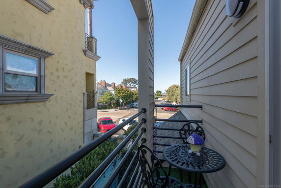 View from a narrow balcony looking out onto a street with parked cars and nearby buildings.