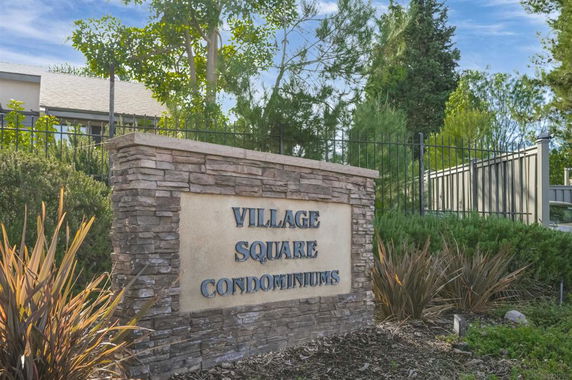 Sign for Village Square Condominiums surrounded by greenery.