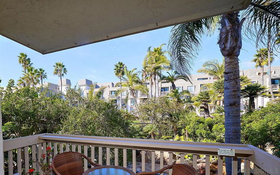 View from a balcony overlooking greenery and modern buildings with palm trees.