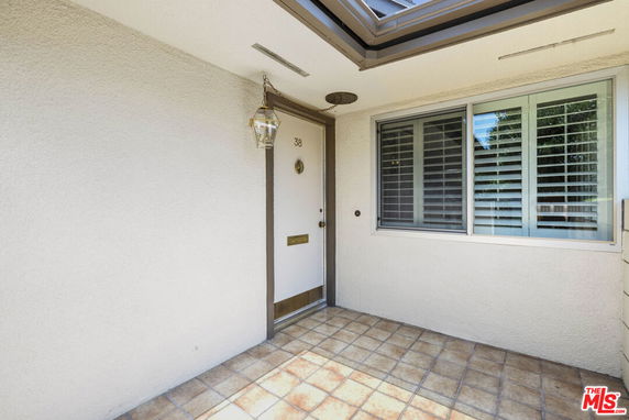 Front entrance of a house with a tiled porch and window shutters.
