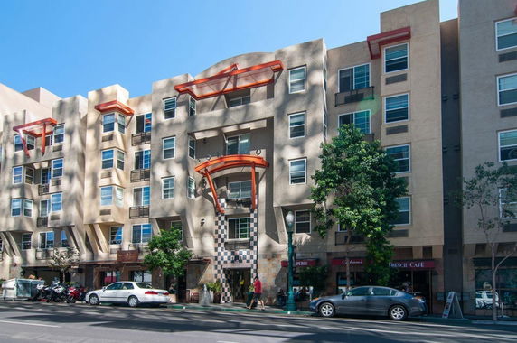 Front view of a multi-story apartment building with balconies and ground floor shops.