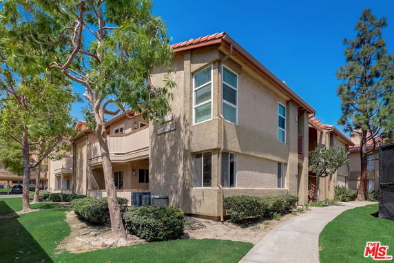 Front view of a two-story apartment building with beige stucco walls and a red tiled roof.