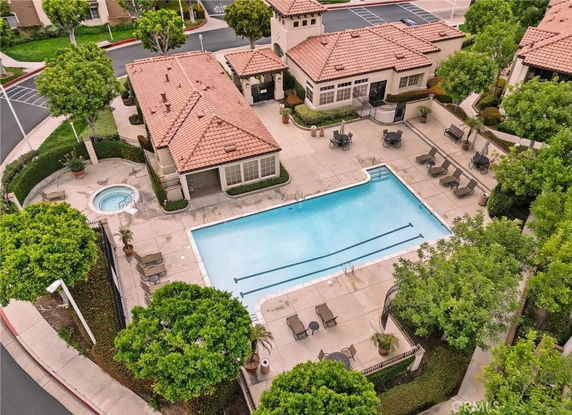 Aerial view of a complex with a swimming pool and hot tub, surrounded by landscaping and buildings with tile roofs.