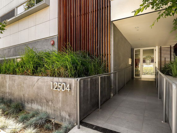 Front view of a modern building entrance with greenery and a concrete facade.