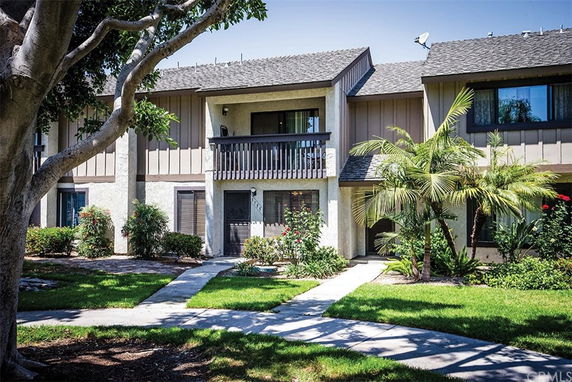 Front view of a two-story residential building with a balcony and a landscaped front yard.
