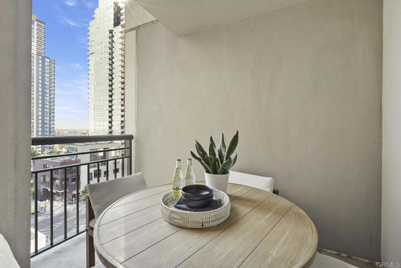 View from a balcony with a round table featuring a small plant and bottles, overlooking high-rise buildings.