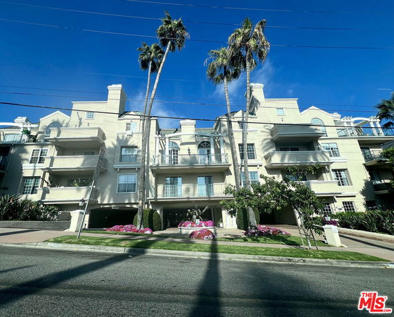 Front view of a multi-story residential building with balconies and palm trees in front.