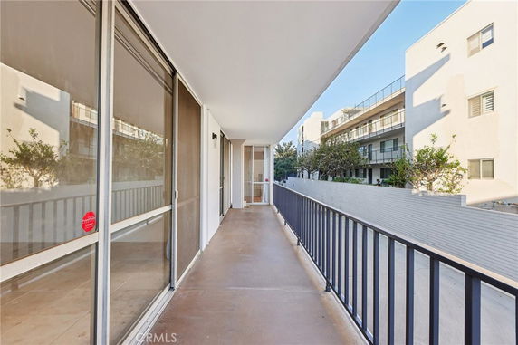 Exterior corridor of a building with railing and large windows, facing other apartment buildings.