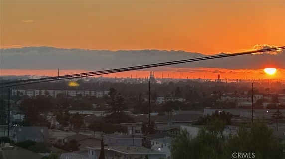 Panoramic view of sunset over a cityscape with distant buildings and smokestacks.