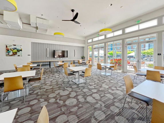 Recreational room with tables and chairs, large windows, and overhead lighting.